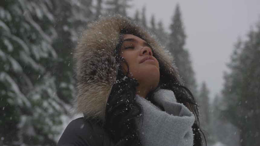 A woman looks up into falling snow