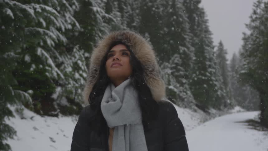 Woman walking down a snow covered road through a forest