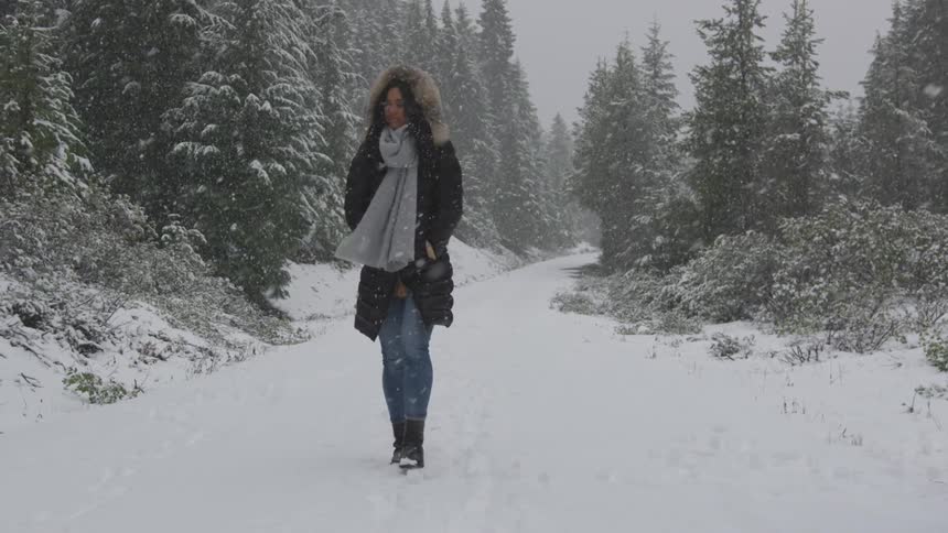 Woman walking down a forest road while snowing