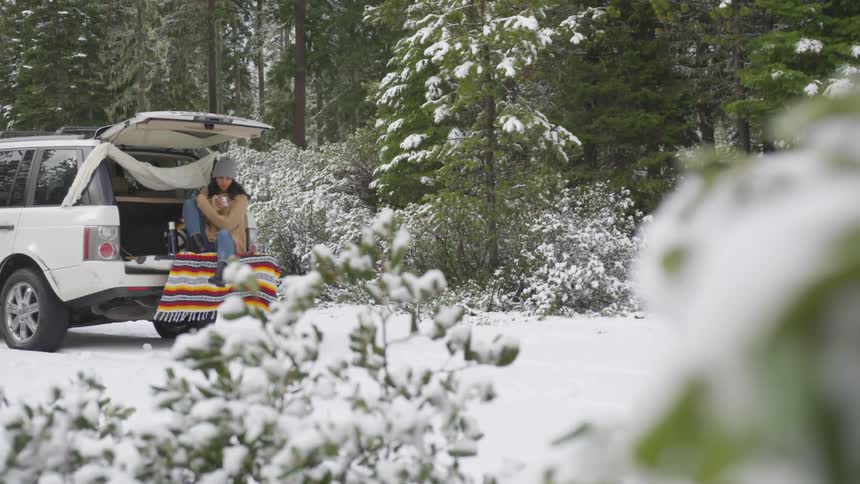 Woman sits in back of hatchback among snow covered trees