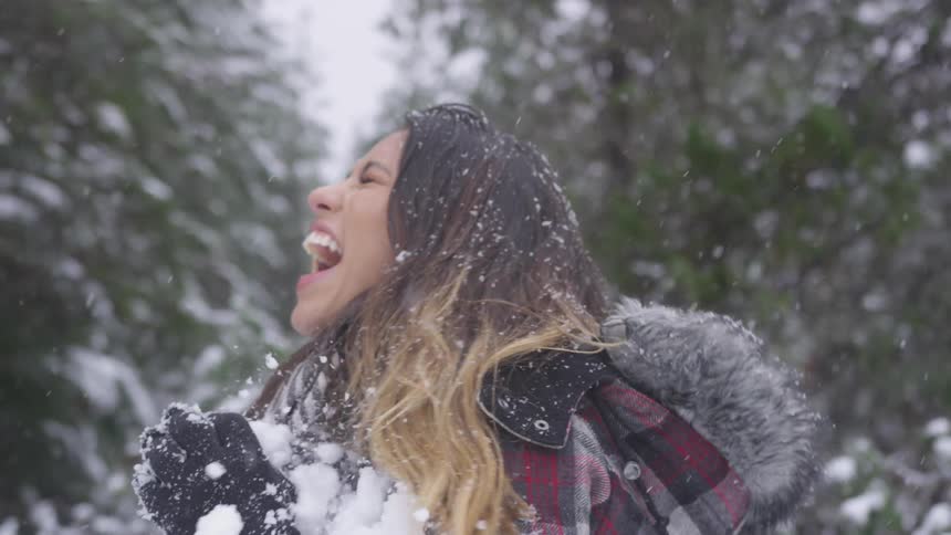 A hispanic woman in a winter coat gets hit with a snowball in the chest