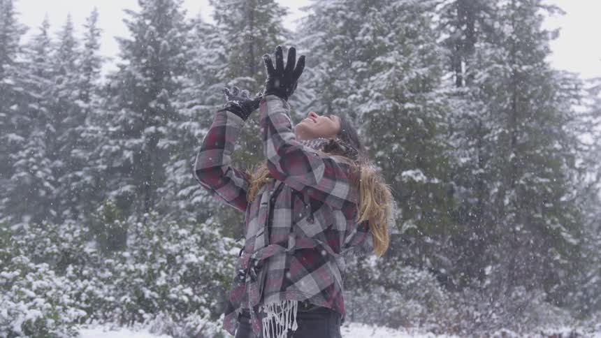 A young girl looks up as she throws a snowball in the air and then catches it