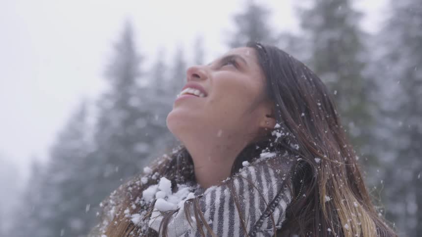 Woman stands outdoors looking up as snow falls