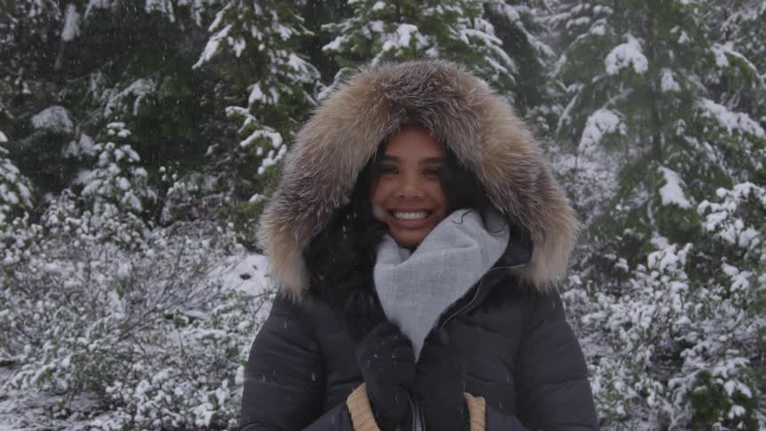 Woman standing under light snowfall on a forest