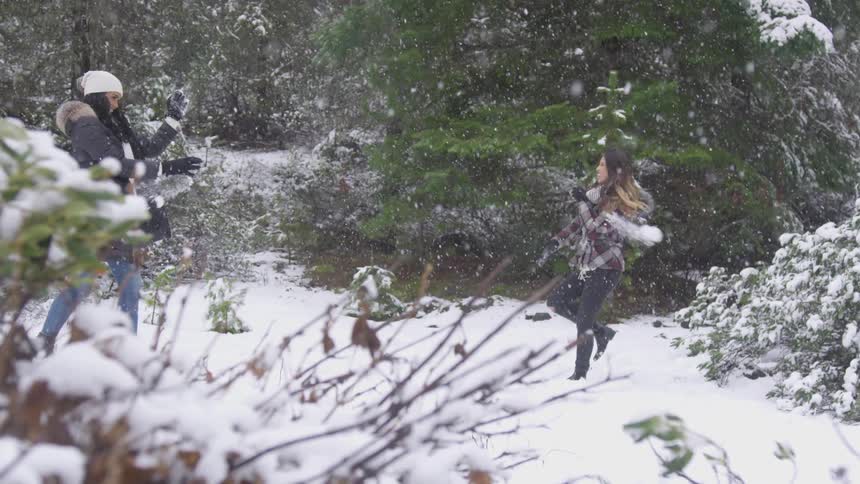 Two women having a snowball fight while snowing in the mountains