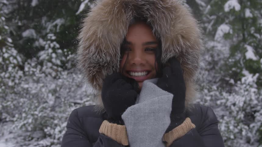 A woman wearing a parka stands in the snow and smiles