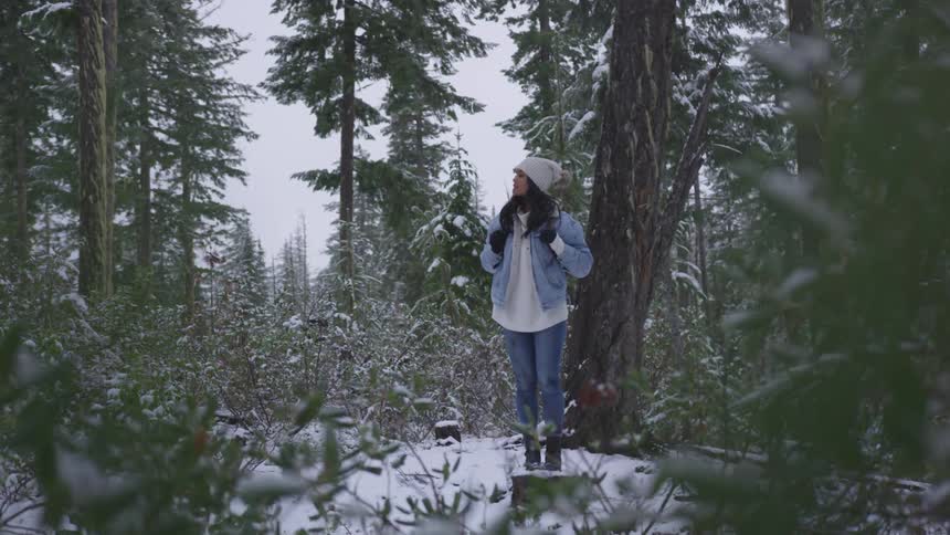 A woman in a coat and winter hat hikes in a snowy forest