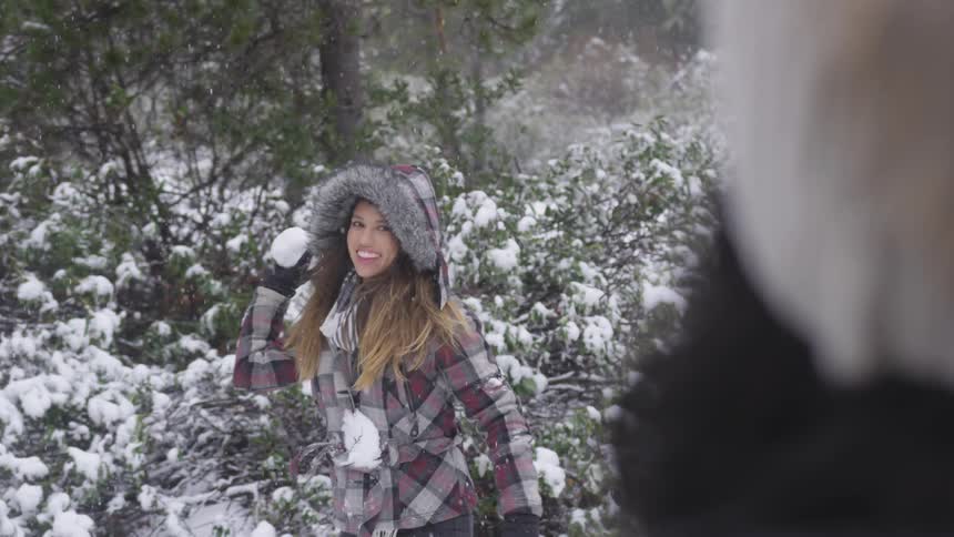 Woman stands in snow and throws a snowball