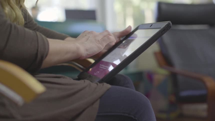 Woman scrolls on a tablet as she sits in a chair