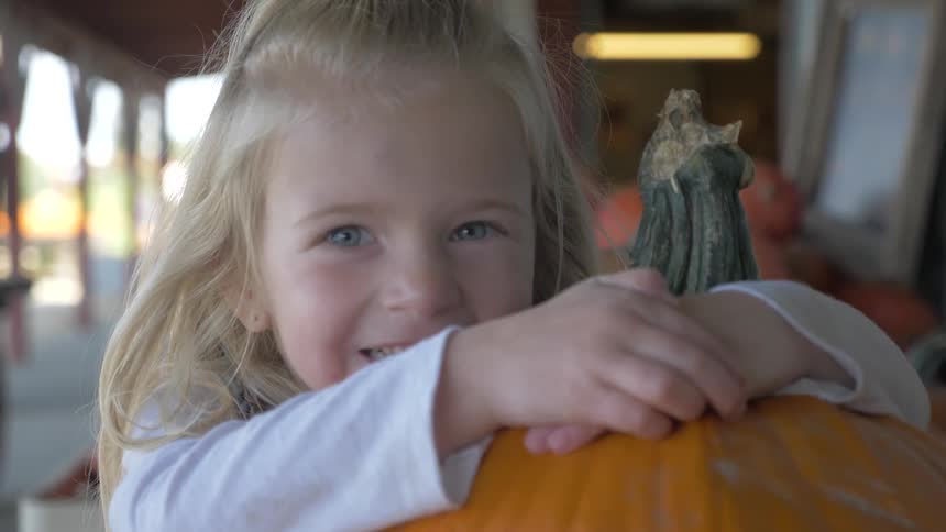 A young blonde girl smiles while hugging a large pumpkin