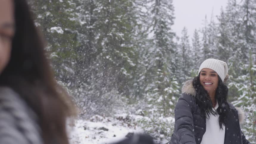 One young woman throws a snowball at another young woman outside in the snow