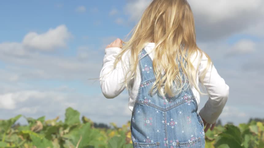 Blonde little girl walks in the farm on a sunny day with cloudy sky
