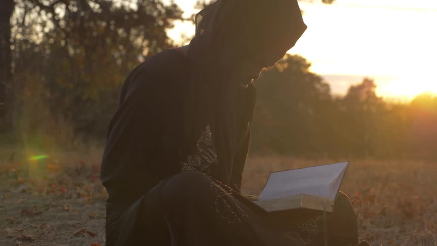 A person sitting in a field reading a book