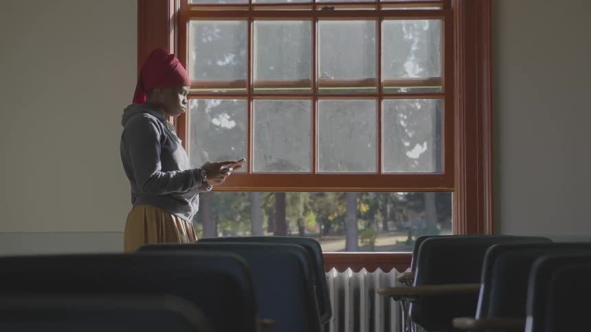 A black woman using standing near a window while using a tablet