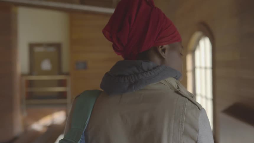 A black woman with a head scarf walks through a room