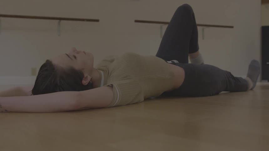 A young woman laying on the floor warming up before dance class
