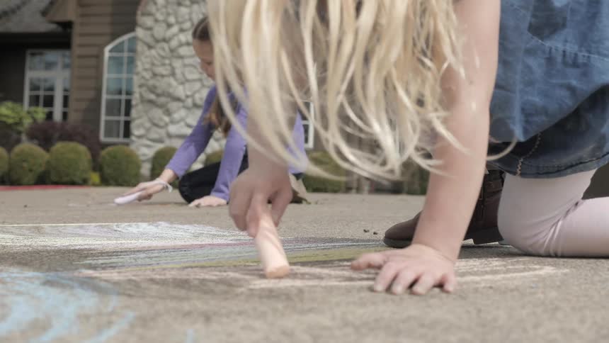 Two young children draw on a driveway with chalk