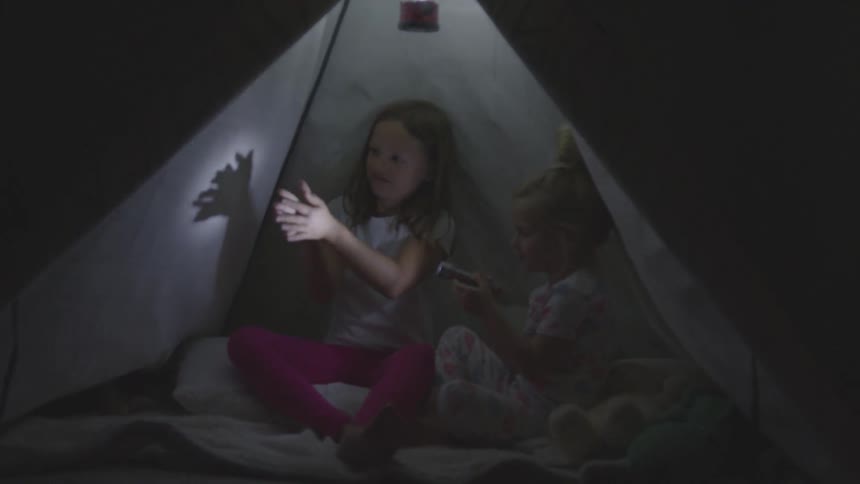 Two children make shadows with a flashlight in the tent