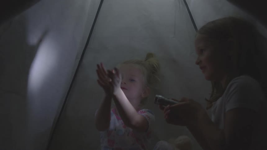 Two white children make shadow puppets inside a tent