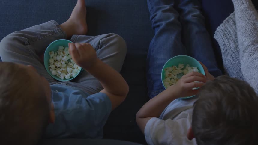 Kids eating popcorn while sitting on a sofa