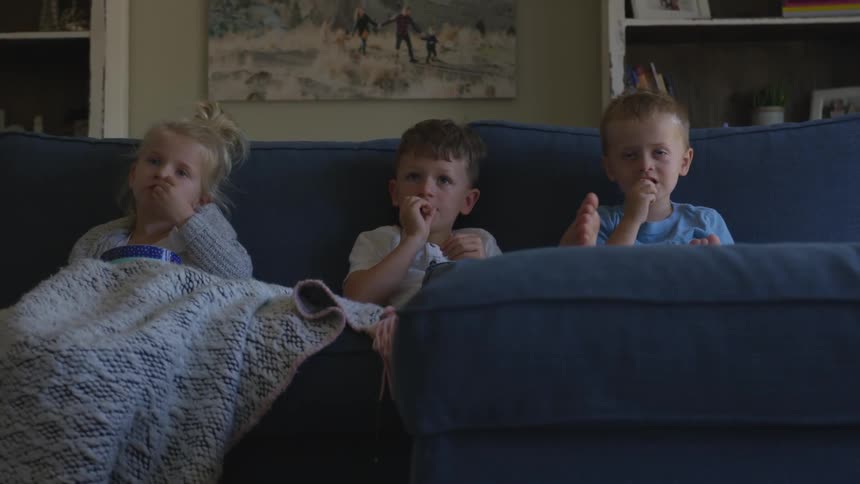 Three children sit on a couch and eat
