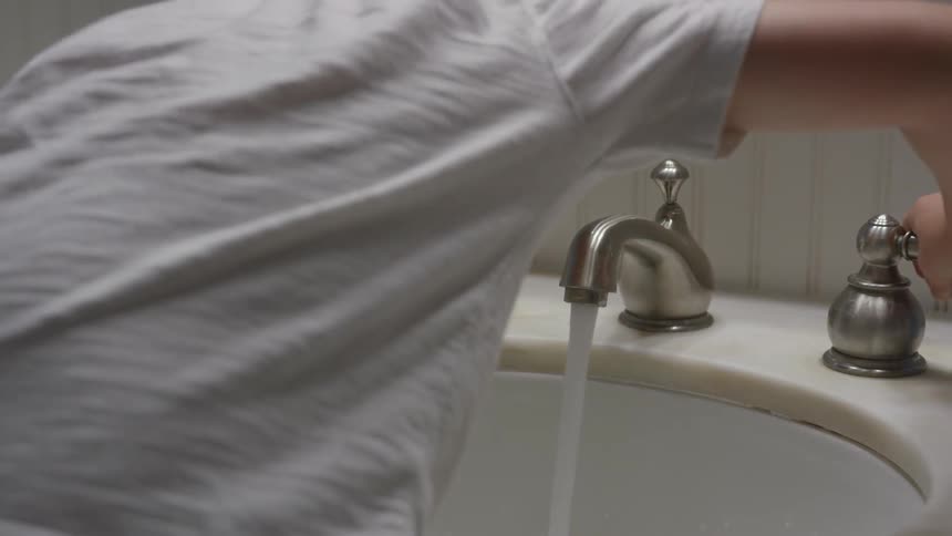 A child turns on a sink faucet and spits into the sink