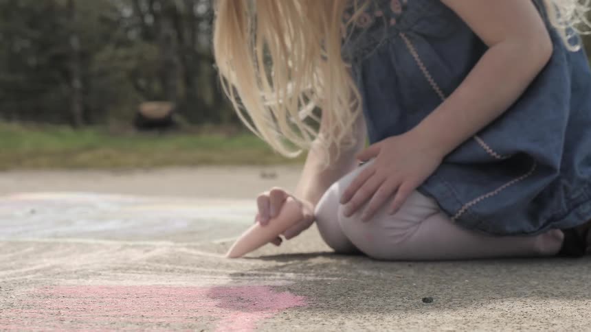 A young child writes on concrete using chalk