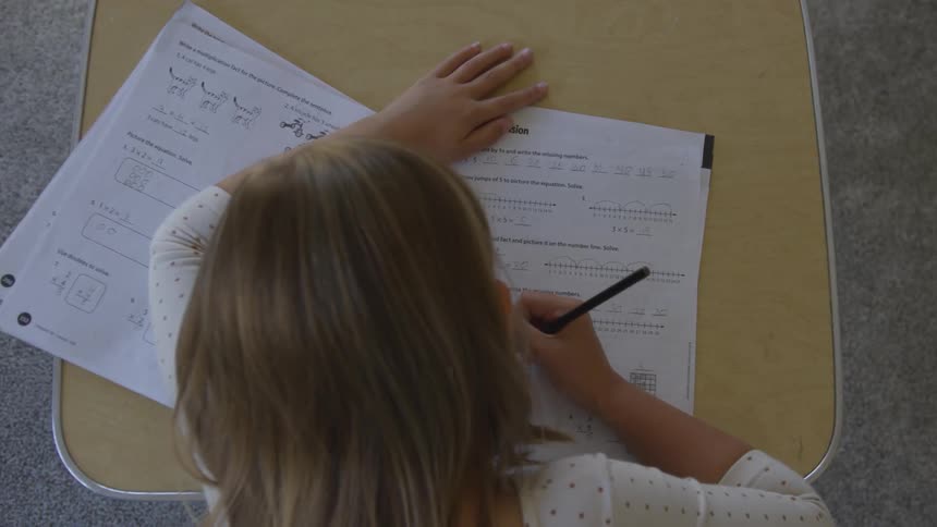 A young girl doing school work at a small desk