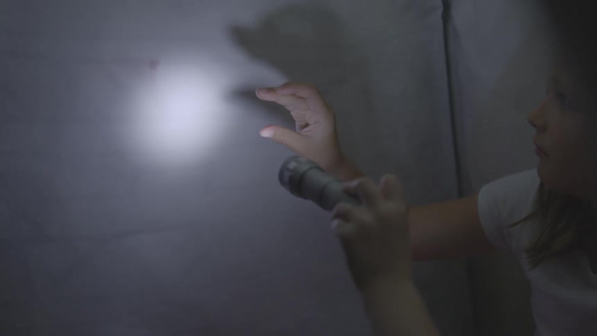 Girls using a flashlight to make hand shadows inside a tent