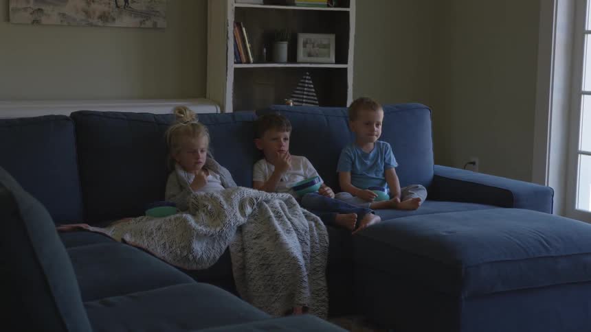 Small children sitting on a blue couch in family room watching tv