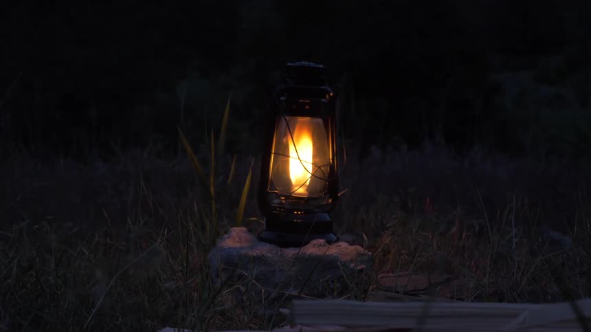 A lantern sitting on a rock with a flame burning within at night