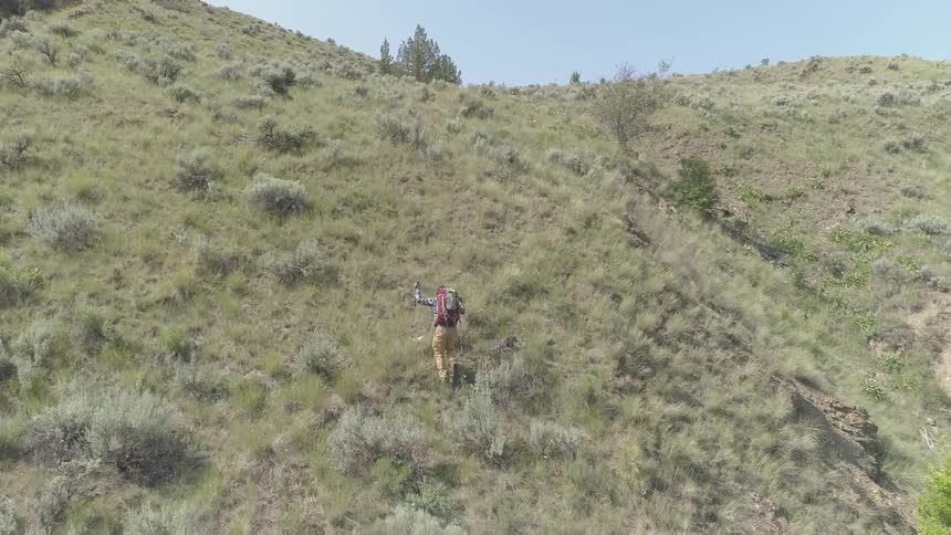 Man wearing backpack walks uphill on a cloudless sunny day