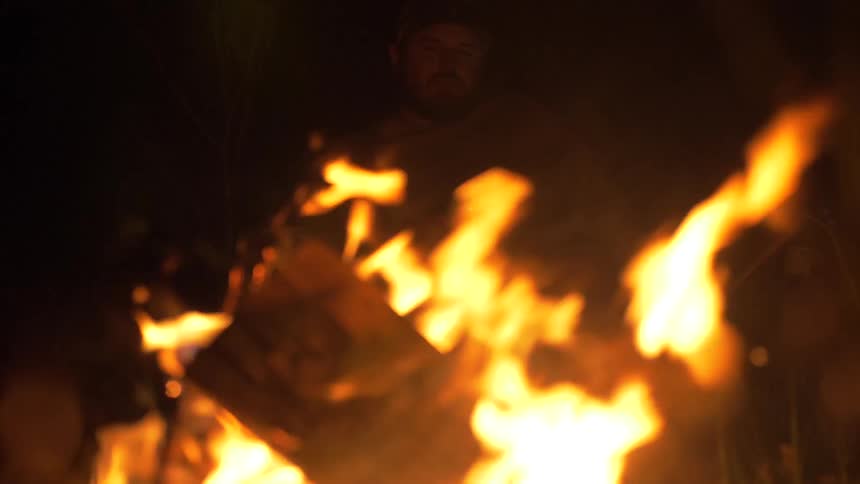 A man sitting in the darkness before a campfire