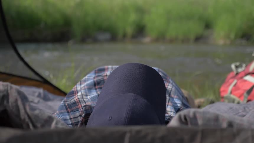 A person sleeps while camping next to a flowing river