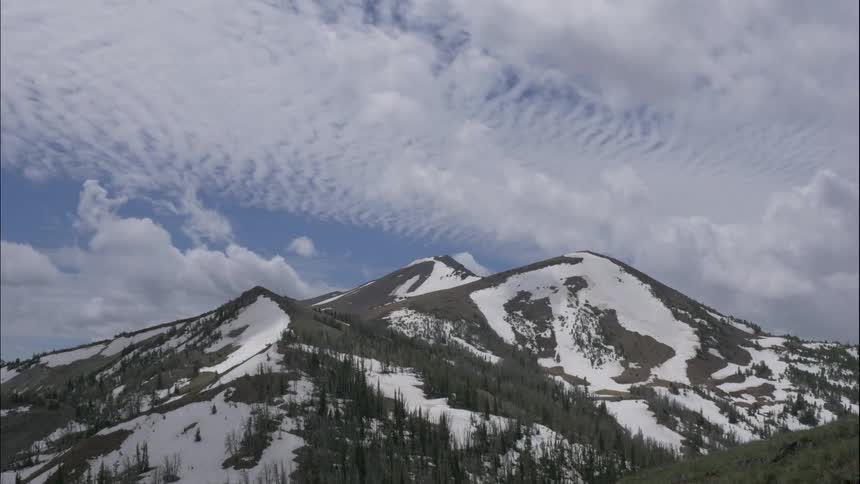 Clouds float past a snow covered mountain