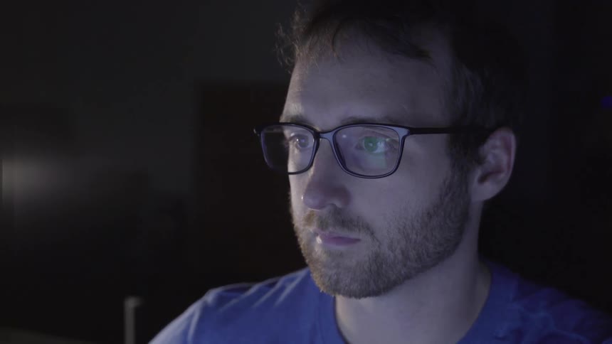 A sad looking white man wearing glasses stares into a screen