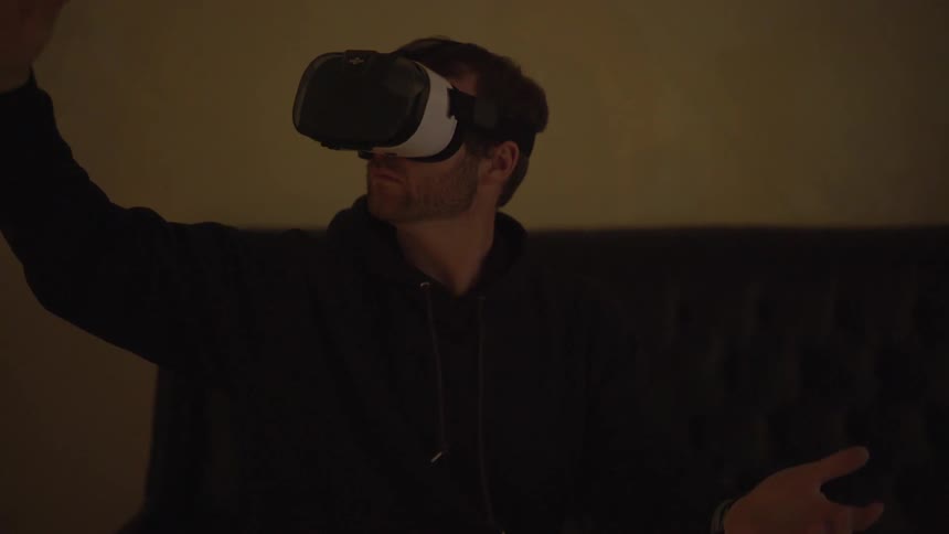 A man waves his arms around and up while using a virtual reality headset