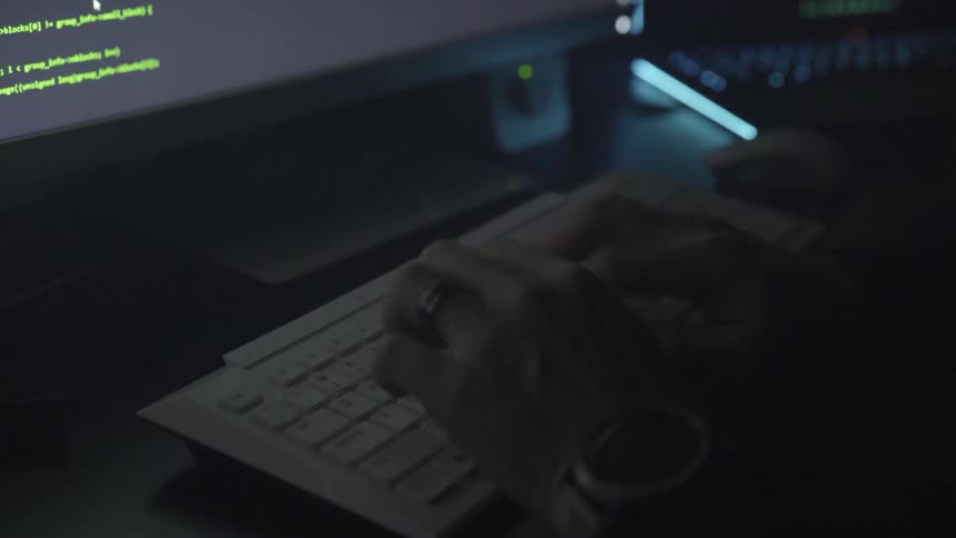 A man typing at a computer in a dark room