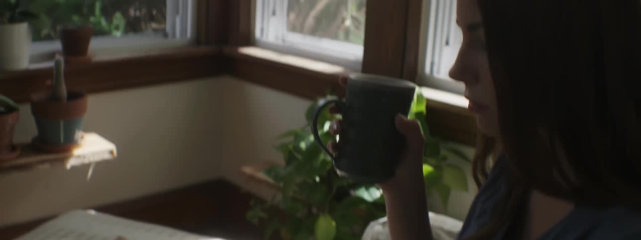 A woman sits and sups from a mug while reading a book