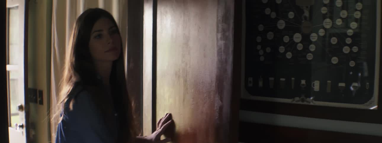 A young woman enters a room and turns to close the door behind her