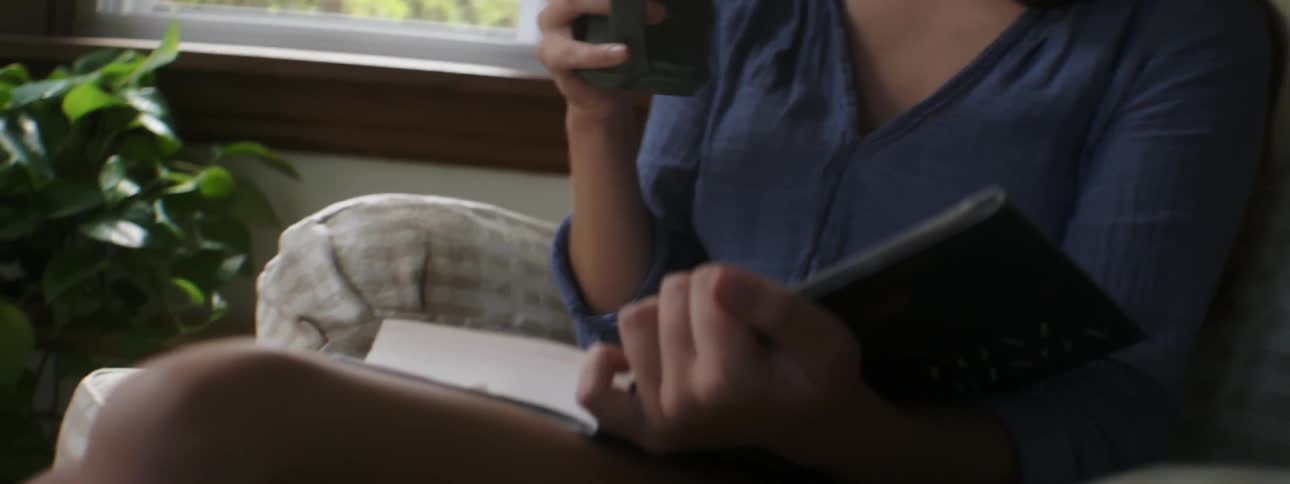 Woman drinking from a mug reading a book
