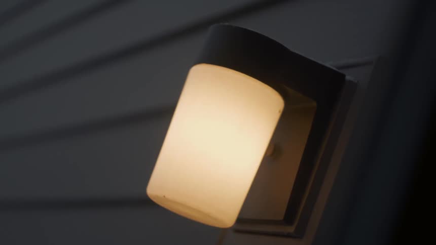 An outdoor light flickering on and off as it snows