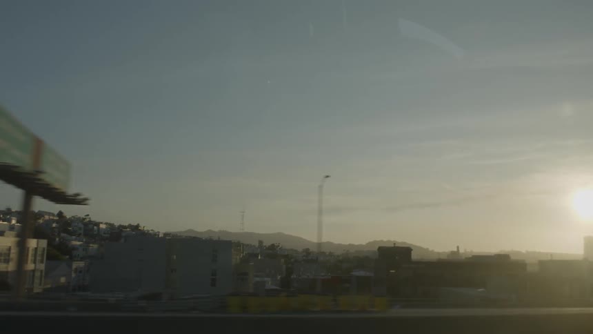 The camera drives down a road looking out over a city