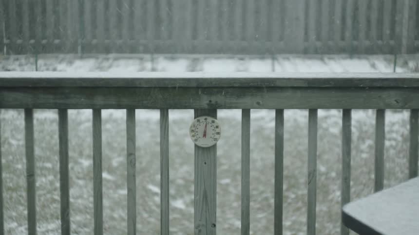 Snow falls down on a railing and the ground