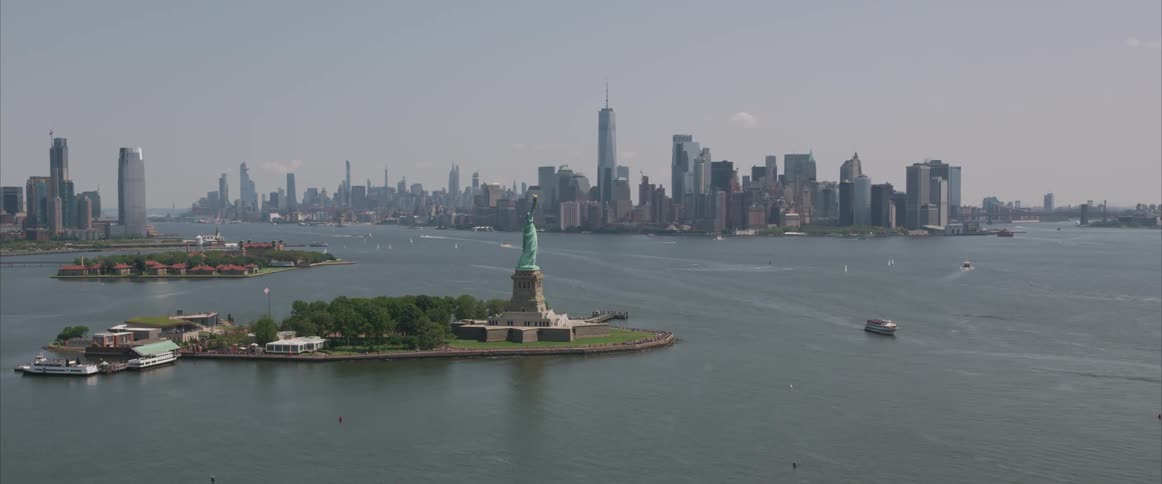 The new york city skyline stands behind the statue of liberty