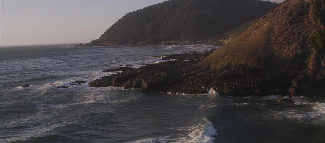 Waves crash against shore near mountains