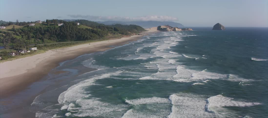 Waves crash on beach near hills and town