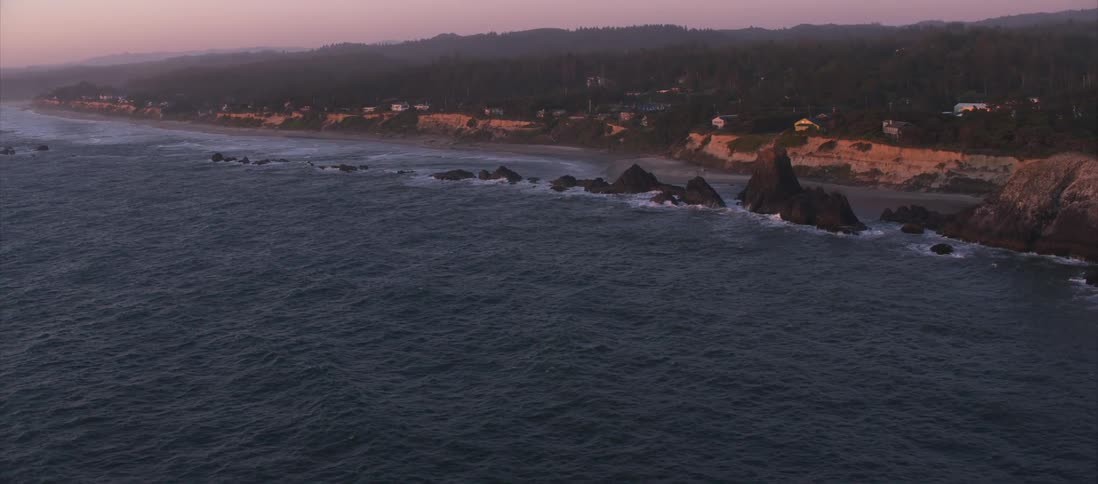 The camera flies over a coastal area with houses in the distance