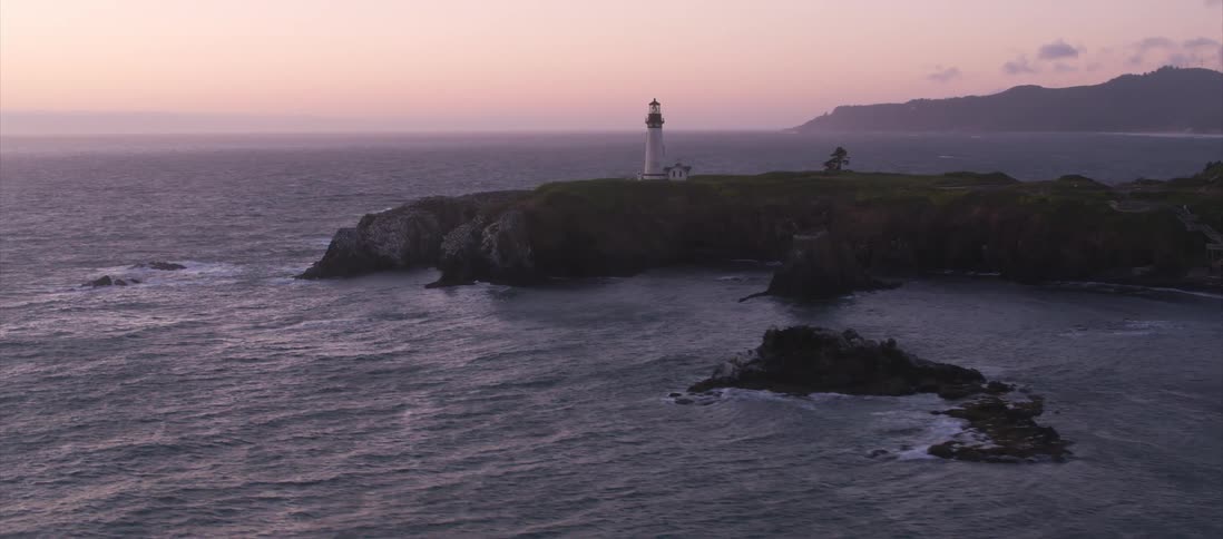 The camera looks at a lighthouse next to the ocean