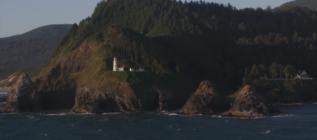 A lighthouse sits along a low rock coast line